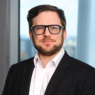 Man with brunette hair and beard, wearing black glasses, white shirt and black jacket